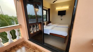 A balcony with a wooden floor and white balustrade, a ceiling fan, and a bed with white bedding. - Sai Sharad Hotel  (Pernem)