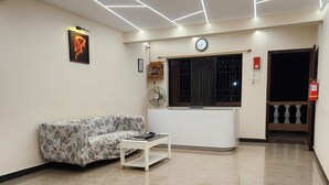 A spacious lobby with a patterned floor, a reception desk, a clock, and a fire extinguisher. - Sai Sharad Hotel  (Pernem)