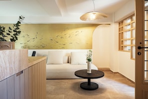 Un interno moderno con una scrivania di legno per la reception, un tavolo nero tondo con un vaso, un divano beige e un murale di pesci.