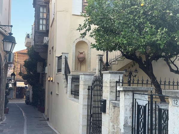 A narrow street with historic buildings, a tree, and a gate with numbers 10 and 12.