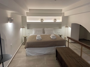 A modern hotel room with a bed, bedside lamps, a bedside table, a bench, and a small table.