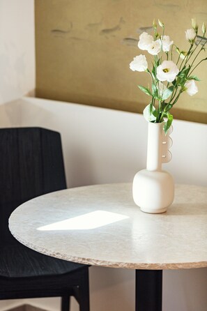 Une table ronde sur laquelle est posé un vase blanc contenant des fleurs blanches.