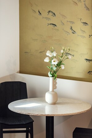 A round table with a white vase containing white flowers, a black chair, and a wall with a fish pattern. - Sea Path VII old town luxury  80 qm 2 Level House a few steps from the beach (Rethymno)