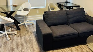 Una sala de estar moderna con un sofá negro, sillas blancas, una mesa de centro de vidrio y un escritorio negro con una lámpara.