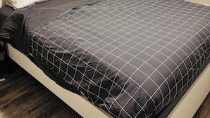 Una cama bien hecha con una colcha oscura estampada y una almohada blanca.