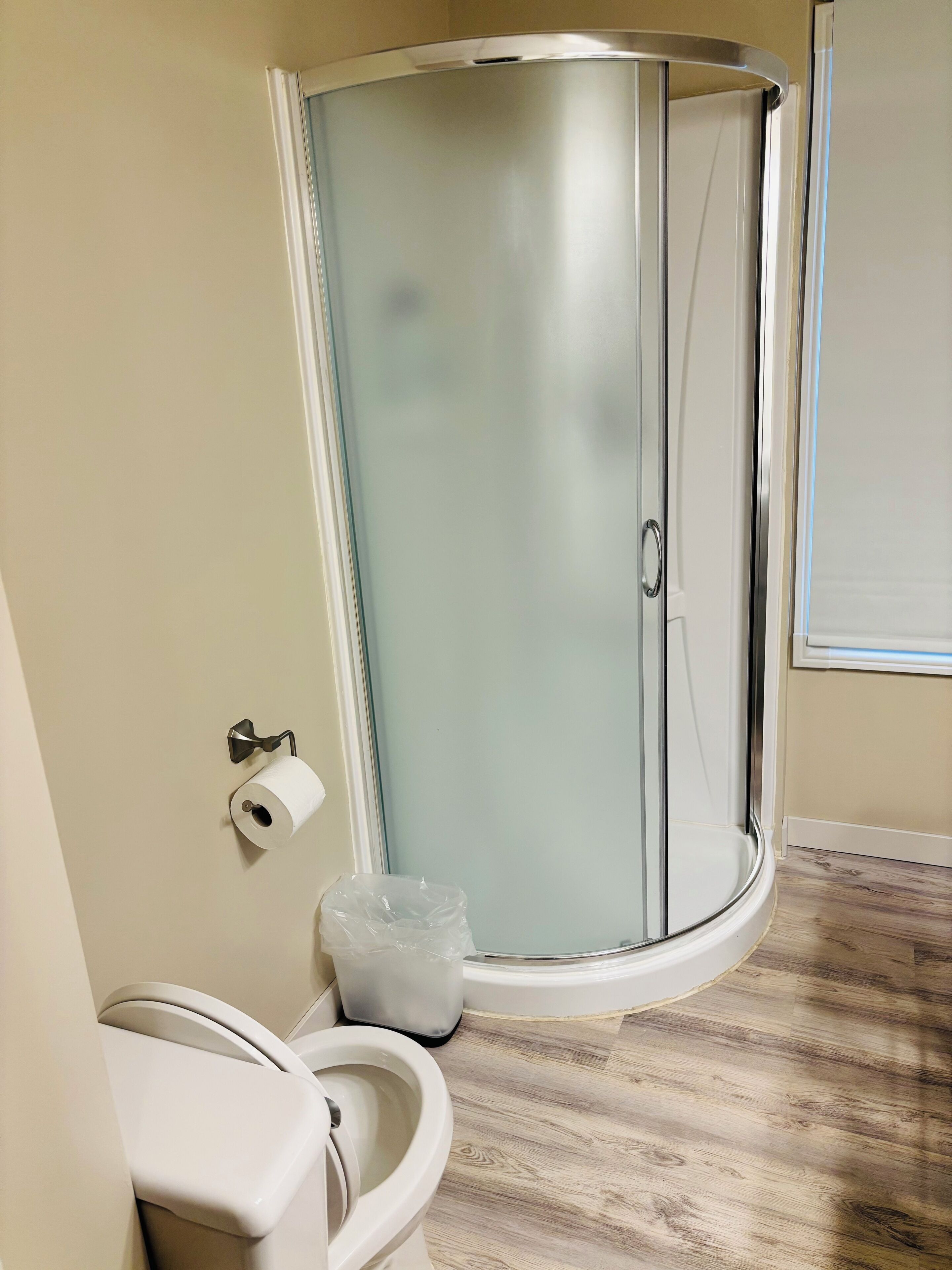 A bathroom with a glass-enclosed shower, a toilet, and a trash bin.