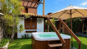 A hot tub with wooden steps, a pergola, and a patio umbrella in a backyard.