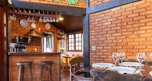 A restaurant with brick walls, wooden bar stools, and a dining area with tables and chairs.