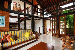 Une pièce spacieuse avec un plafond haut, un canapé à rayures, une table en bois et un escalier.