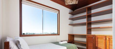 A room with a bed, a window with blinds, a wooden ceiling, and built-in shelves.