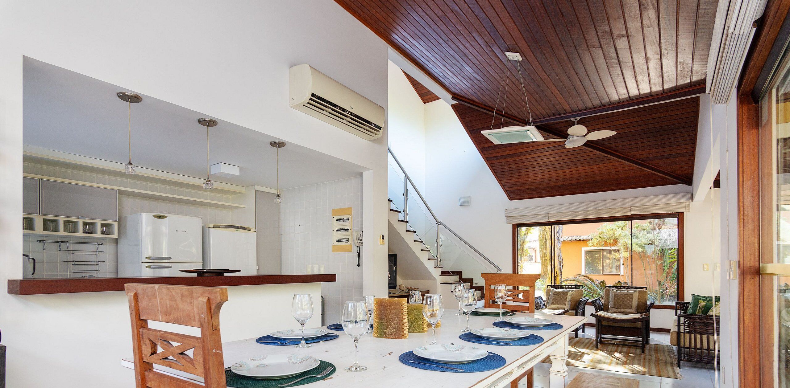 A modern kitchen with white appliances, a dining area with a table set for four, and a staircase leading to a balcony with outdoor seating.