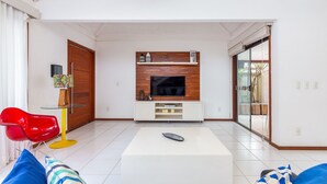 Una sala moderna con televisión de pantalla plana, pared decorativa de madera, mesa de centro de vidrio y una silla roja.