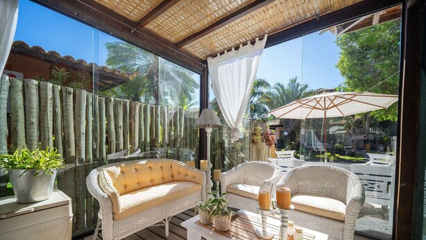 A sunlit patio with wicker furniture, a white table, and a potted plant. - Bz92 Beautiful house 600m from Rua das Pedras! 4 suites (Armação dos Búzios)