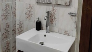 Une salle de bain avec un lavabo blanc, un miroir, un rideau de douche et des carreaux à motifs.