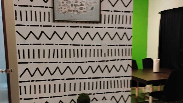 Una stanza con una parete decorata, un quadro incorniciato, un tavolino con una pianta in vaso e una parete verde a contrasto.
