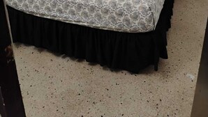 Un letto con una coperta e cuscini a fantasia, una struttura letto nera con gonna e un muro decorato con un motivo a righe semplici.