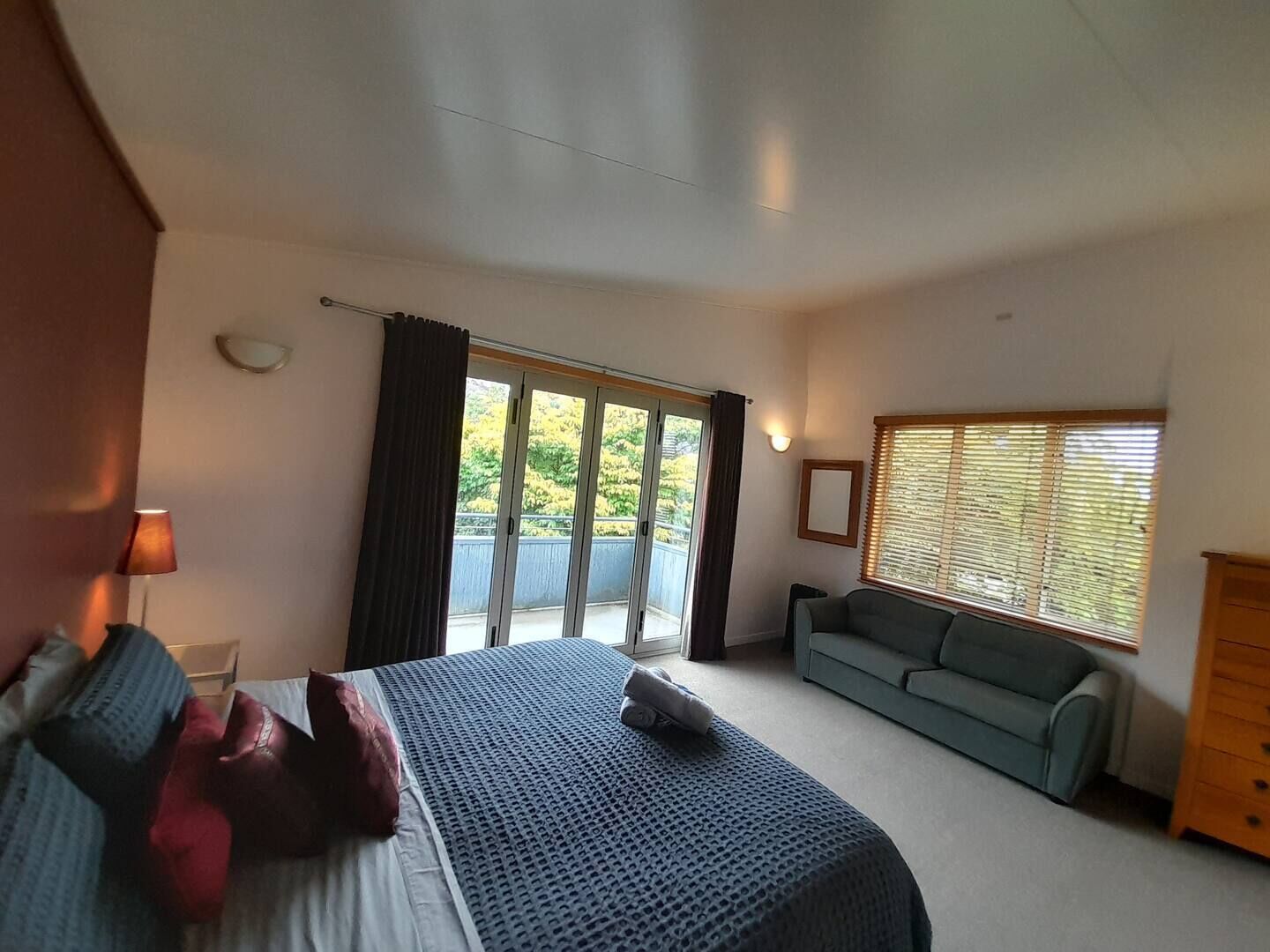 Une chambre à coucher comprenant un lit, un canapé, une commode et une fenêtre avec des stores.