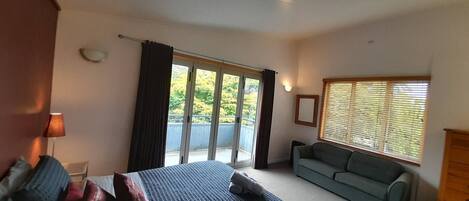 A bedroom with a bed, a sofa, a dresser, and a window with blinds.