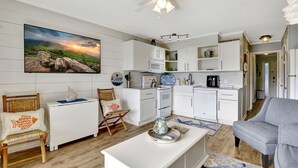 A modern kitchen with white cabinetry, a ceiling fan, and a large flat-screen TV mounted on the wall. - Charming beachfront villa in Hilton Head Island with pool, beach/pool bar & more (Hilton Head Island)