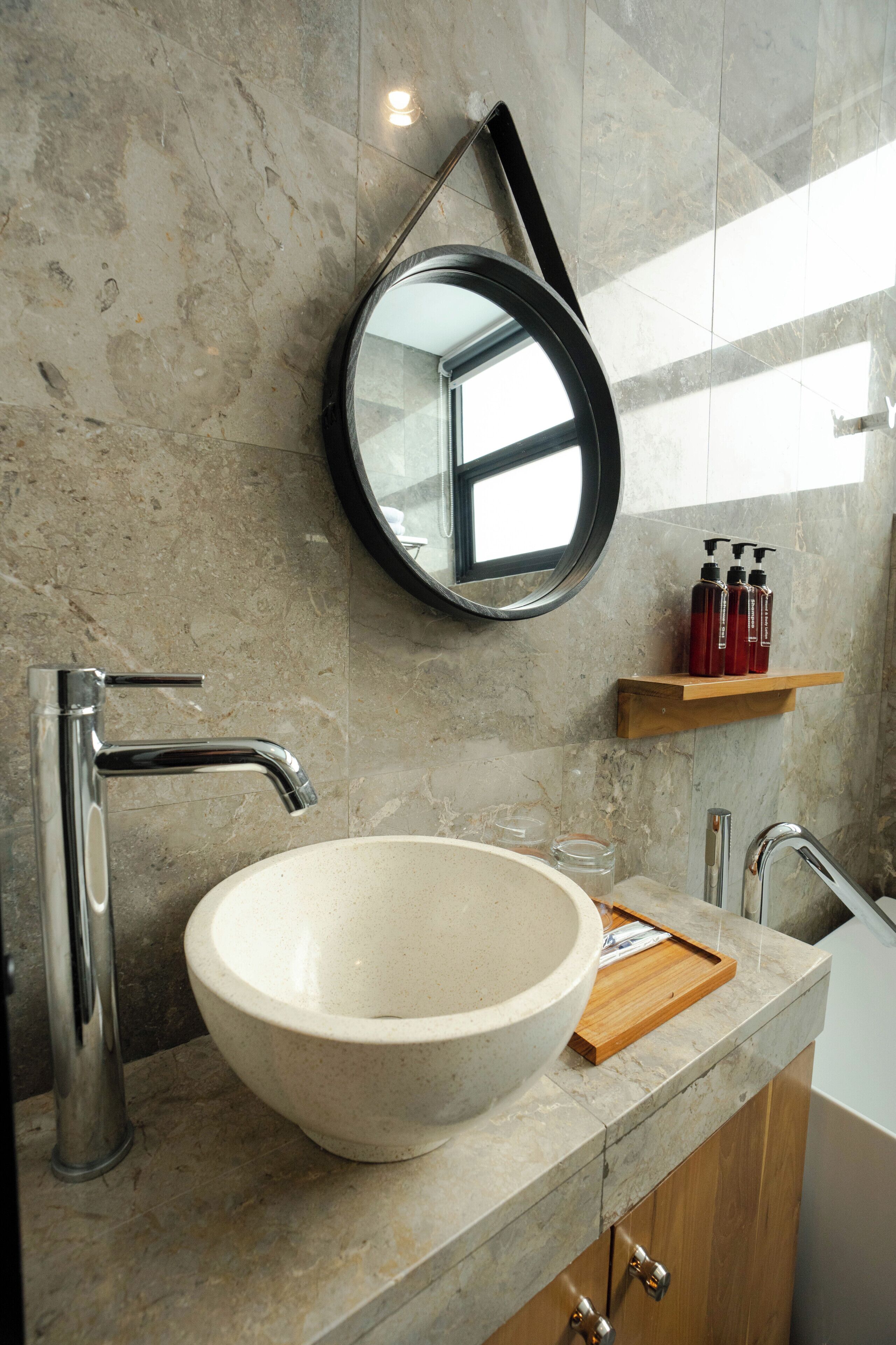 Une salle de bain avec un grand lavabo rond, un miroir et une étagère en bois où sont posées des bouteilles.