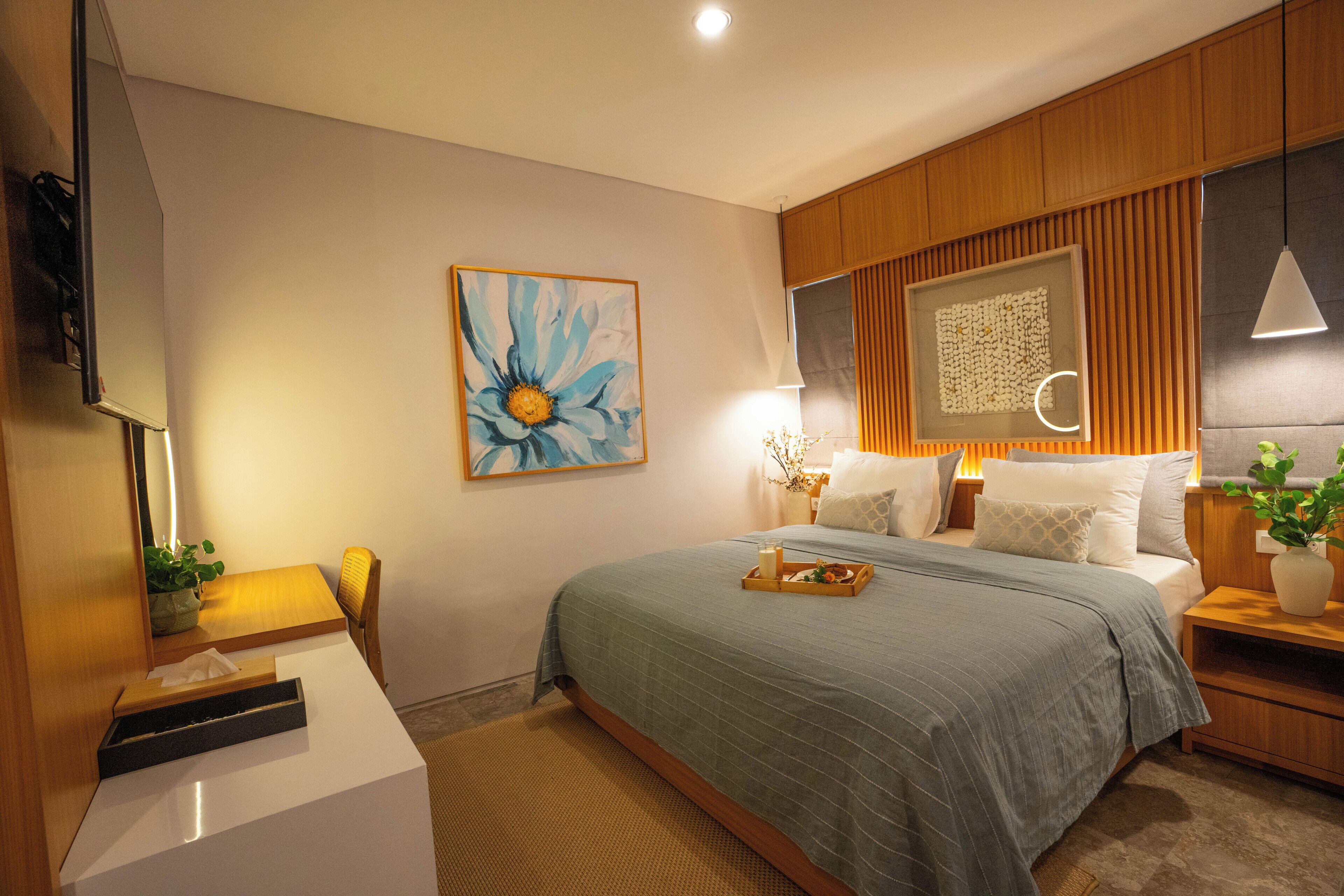 Un dormitorio moderno con una cama grande, mesitas de noche, un escritorio y un televisor montado en la pared.