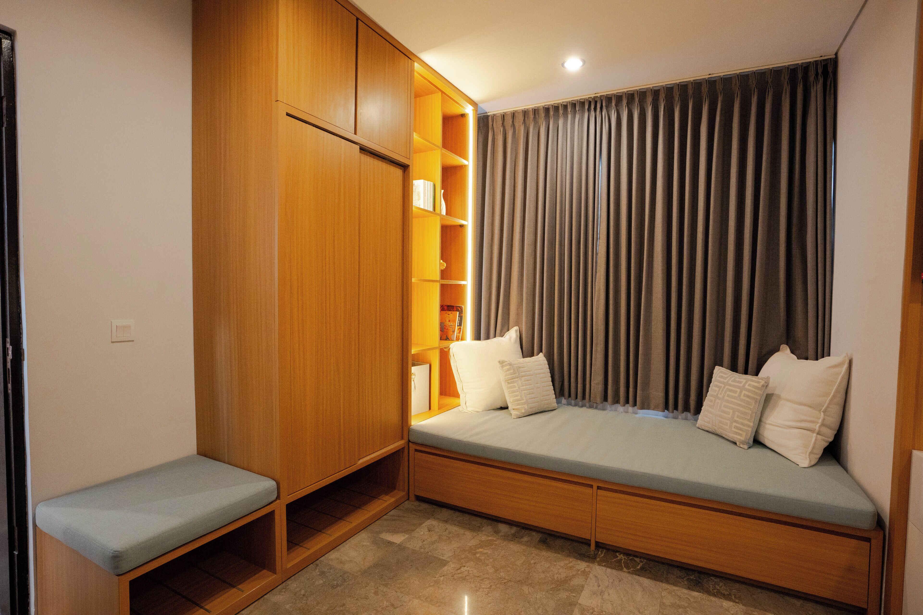 A room with a built-in bench, wooden wardrobe, and a window with curtains.
