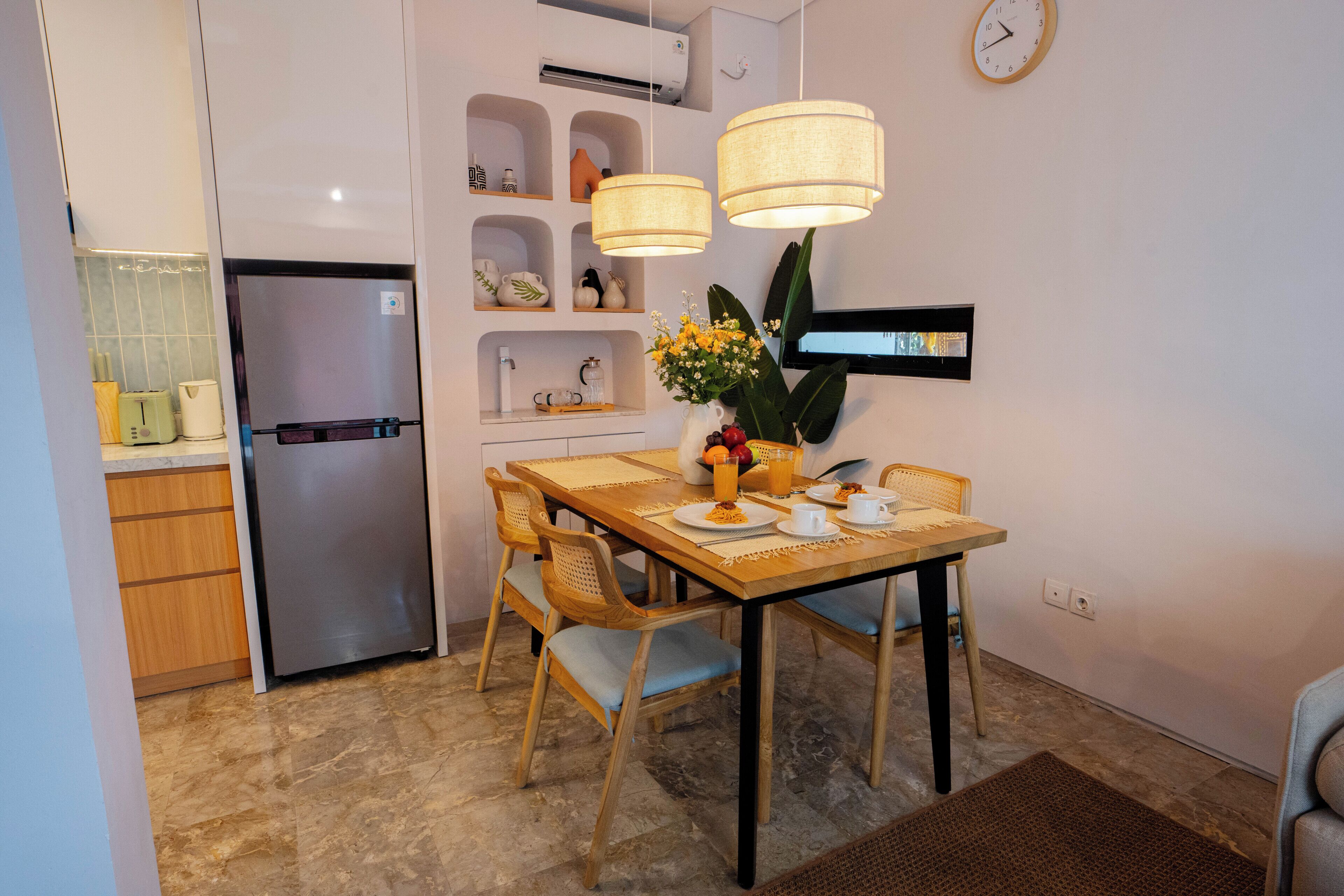 A compact kitchen with a refrigerator, dining table, chairs, and a clock on the wall.