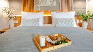 Habitación de hotel con una cama grande, paneles de madera, una obra de arte enmarcada sobre la cama y una bandeja con tostadas y una bebida sobre la cama.