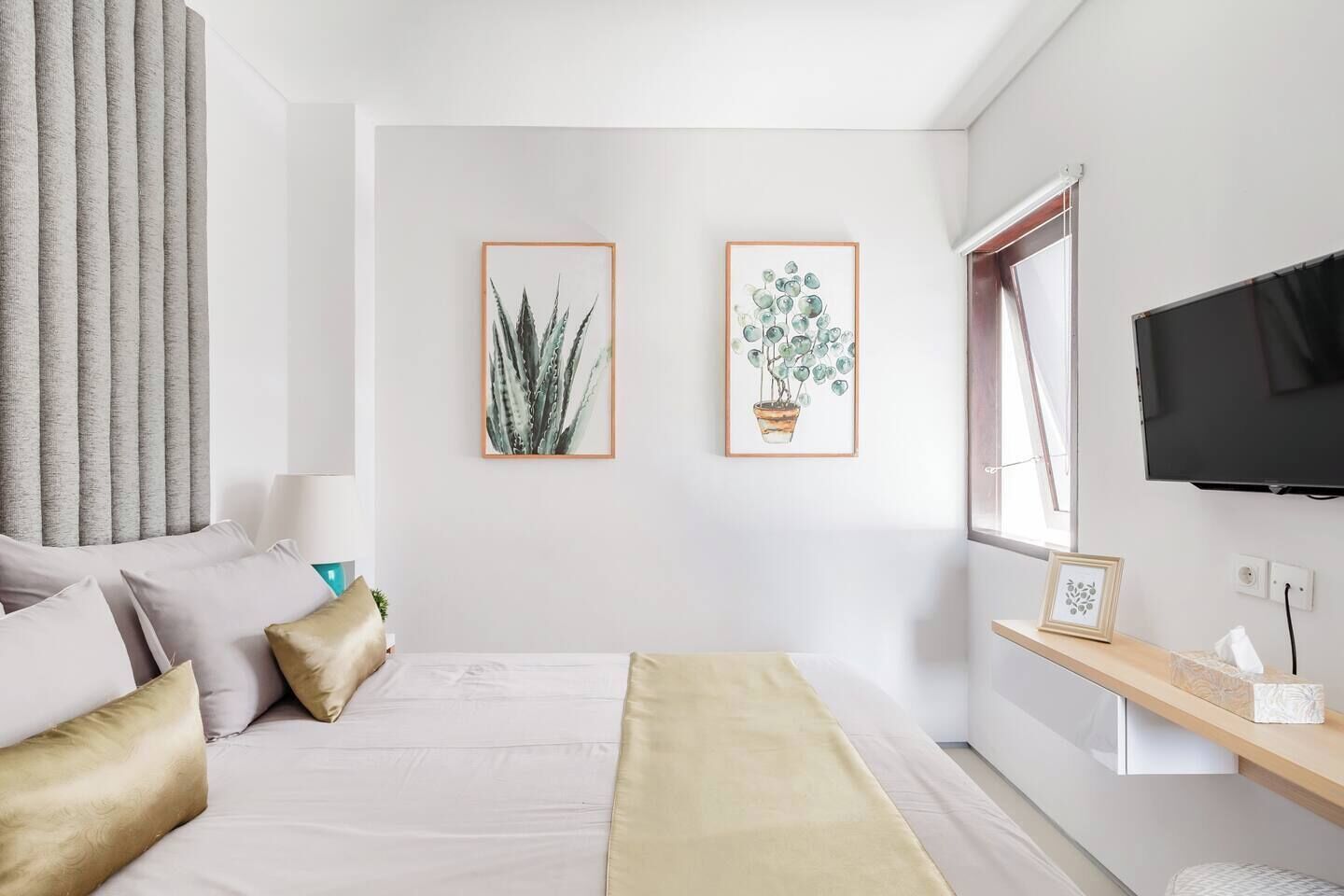 Un dormitorio moderno con una cama, dos obras de arte botánicas enmarcadas, un televisor y una mesita de noche con una lámpara.