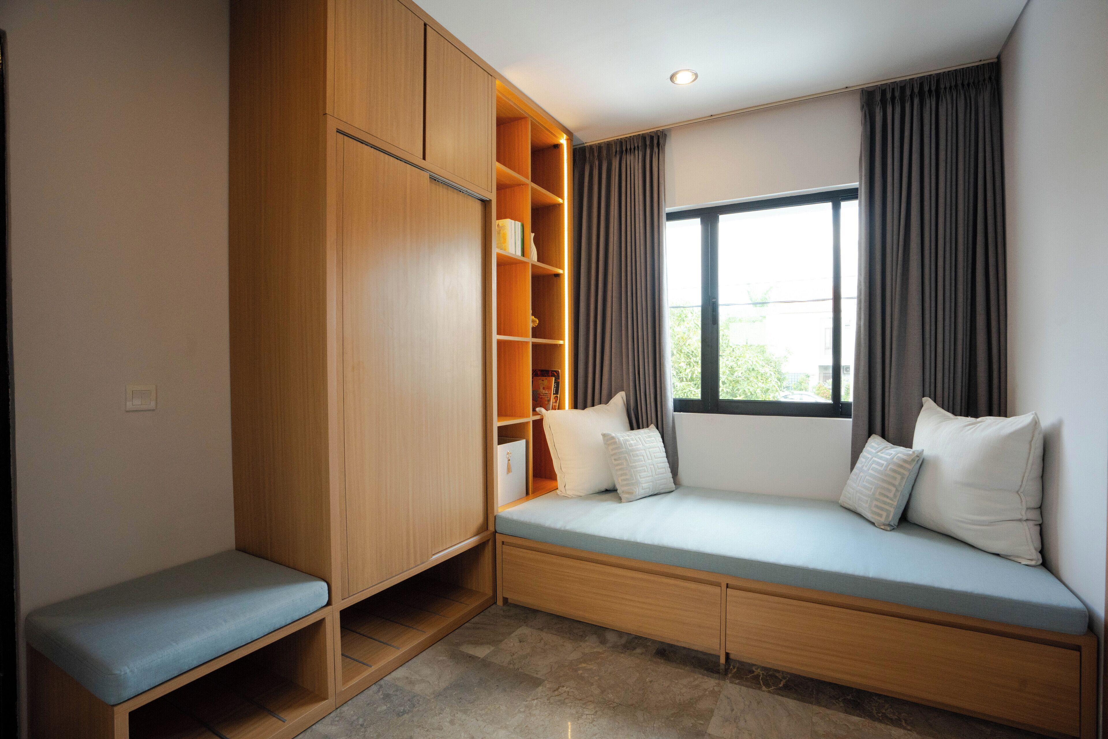 A room with a built-in bench, wooden wardrobe, and a window with curtains.