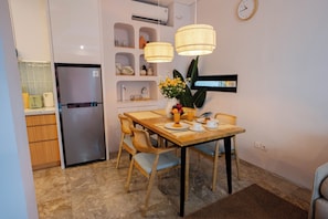 Una cocina compacta con refrigerador, una mesa de comedor con sillas y un reloj en la pared.