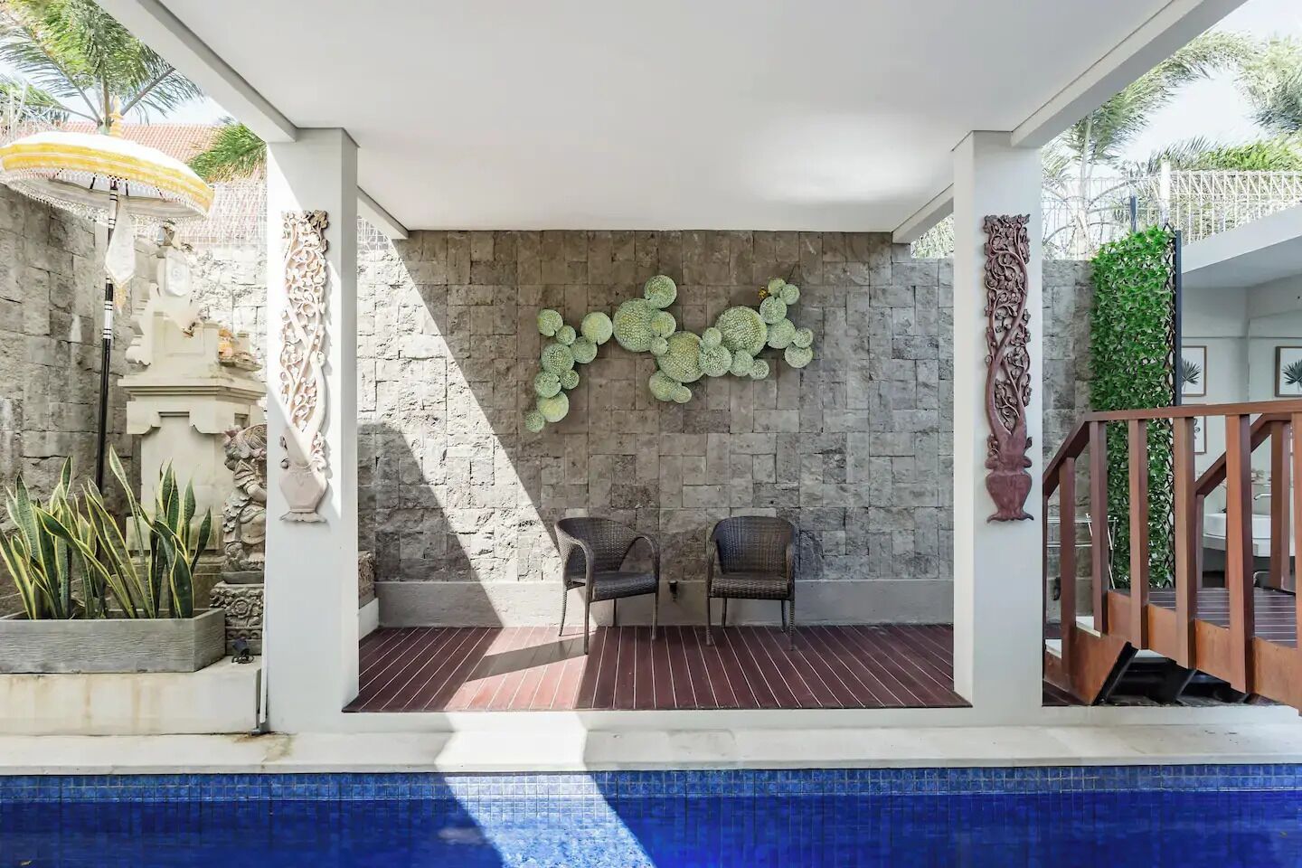 Área de piscina coberta com paredes de pedra, duas cadeiras de vime e uma peça de arte decorativa.
