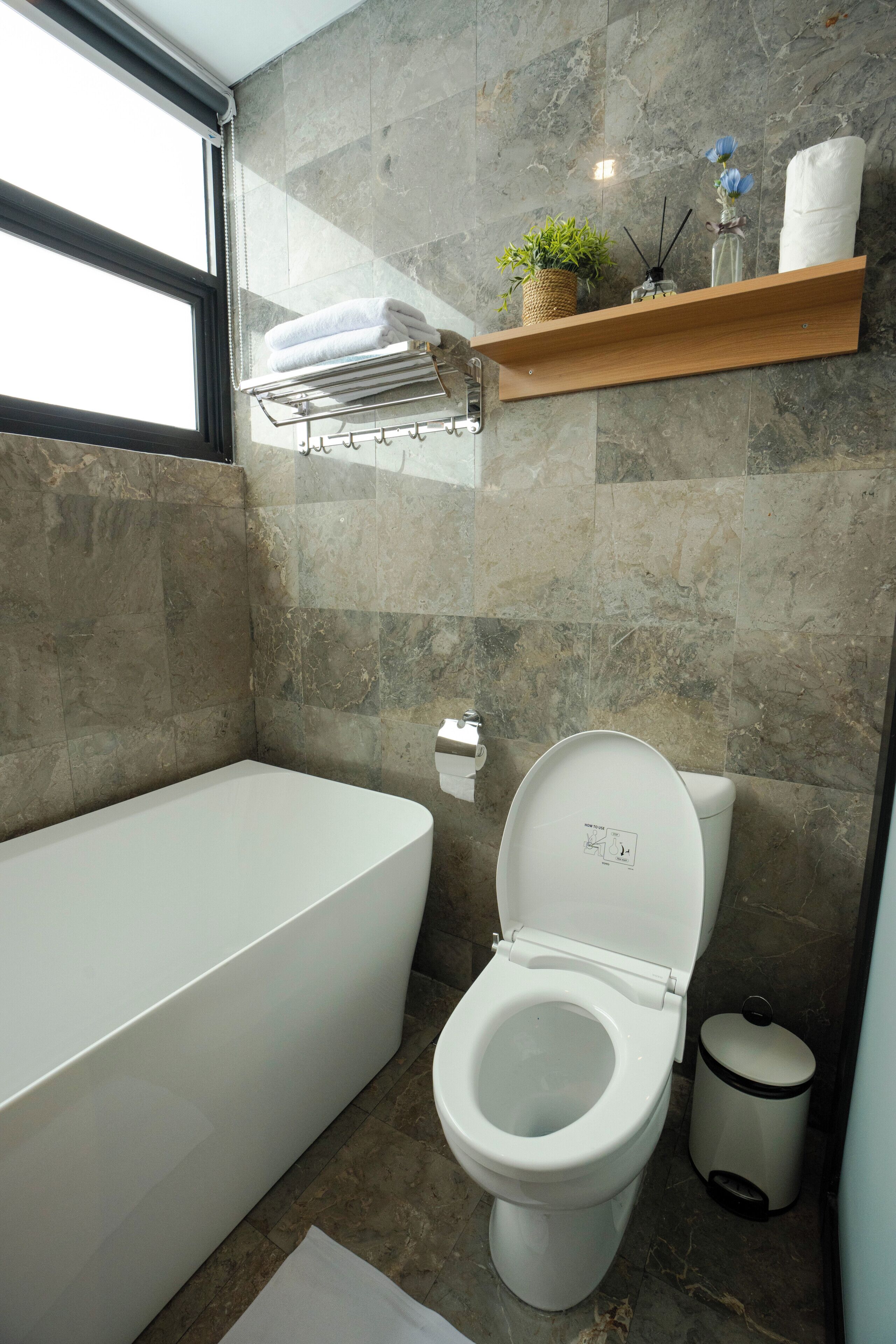Ein modernes Badezimmer mit Badewanne, Toilette und Ablagefläche mit Handtüchern und Pflanzen.