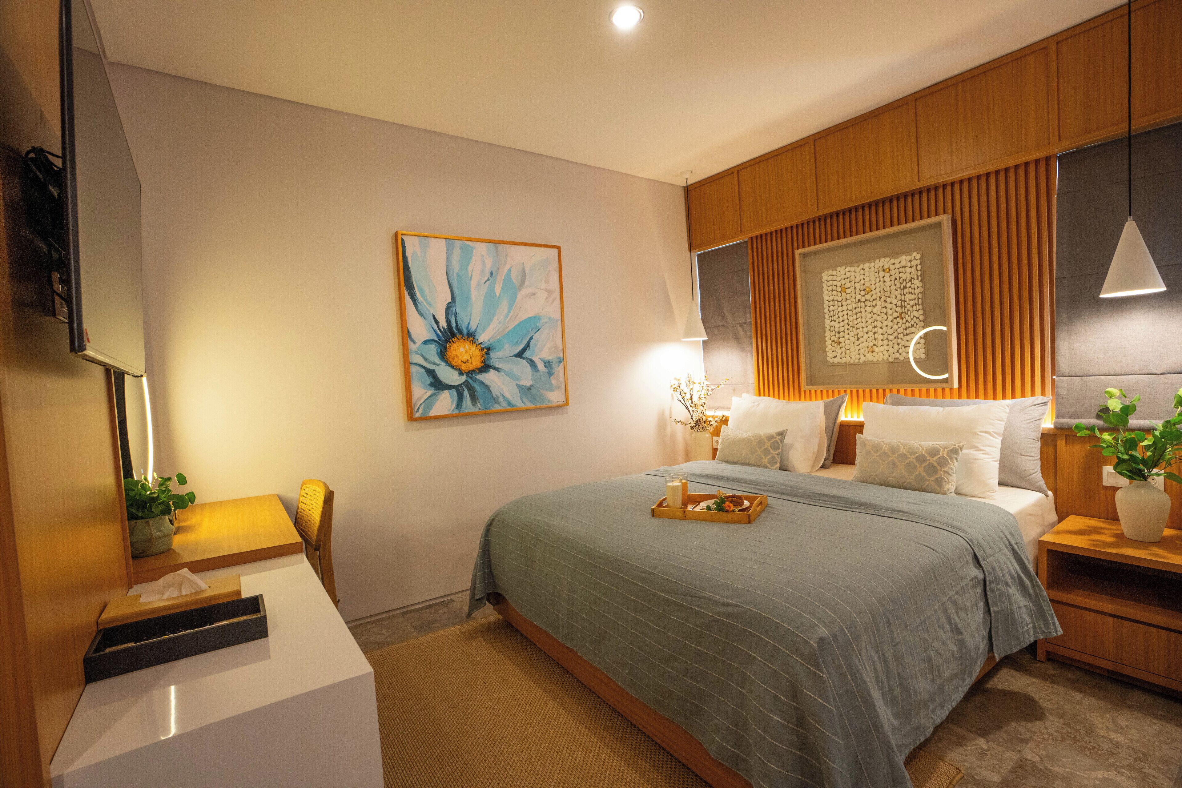 Un dormitorio con cama, mesitas de noche, escritorio, silla, un cuadro y una planta en maceta.