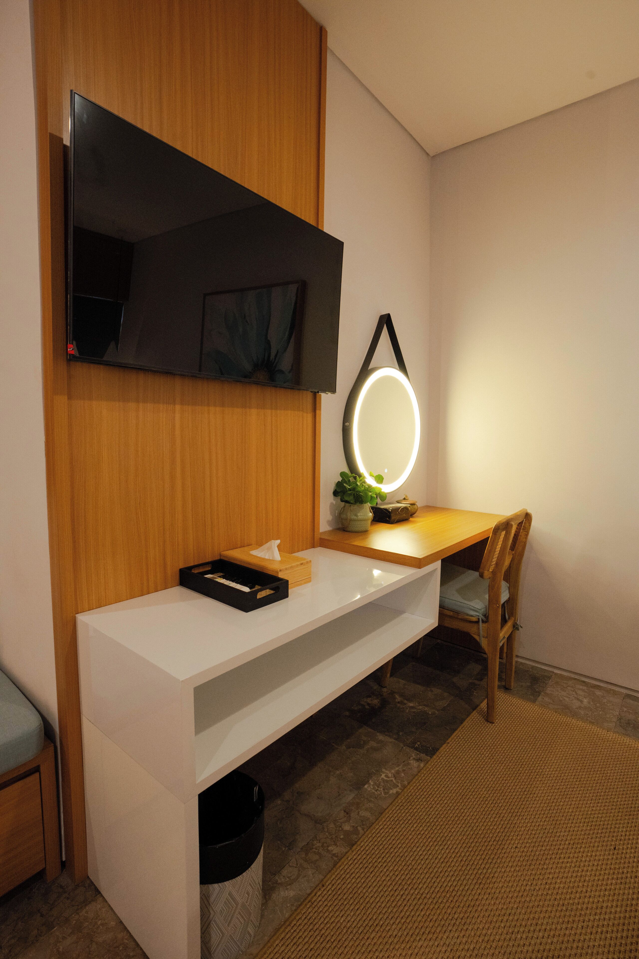 Une chambre moderne avec un bureau en bois, un téléviseur fixé au mur, une table de chevet et une chaise.