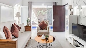 Una sala de estar moderna con sofá, sillón, mesa de centro, televisor y una pared de piedra con diseño geométrico.