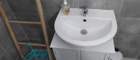 Ein Badezimmer mit einem weißen Waschbecken, einer Bambusleiter und einem blauen Reinigungswerkzeug.