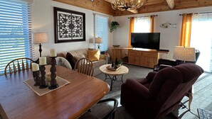 A spacious living room with a wooden ceiling, a large TV, and a dining area with a wooden table and chairs. - Cozy 1-bedroom cabin with AC, WiFi & garage in charming Ironwood (Ironwood)