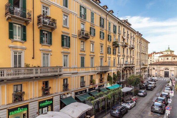 A row of yellow buildings with green shutters, storefronts, and balconies.