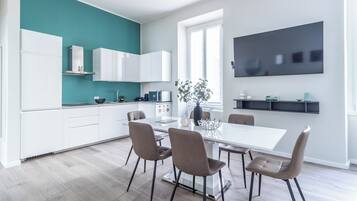 A modern kitchen with white cabinets, a teal accent wall, and a dining area with a white table and four chairs.