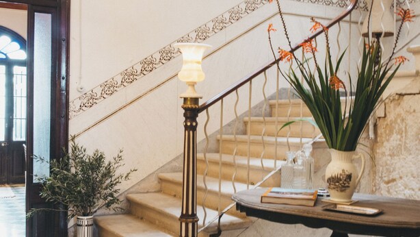 A staircase with a lamp, a potted plant, and a table with a book and a vase. - Joia House is a luxury stately home in Mahon for the best vacation experience (Maó-Mahón)
