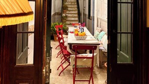 A narrow courtyard with a dining table set for two, surrounded by red chairs, a small staircase, and potted plants. - Joia House is a luxury stately home in Mahon for the best vacation experience (Maó-Mahón)