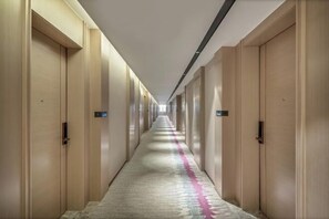 Un long couloir étroit, typique des hôtels, avec des portes en bois de chaque côté, une moquette à motifs et un luminaire au plafond.