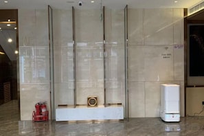 Uma área de recepção com parede de mármore, um extintor de incêndio e um aparelho branco no chão.