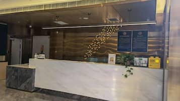 Una mesa de recepción con mostrador de mármol, una planta y carteles informativos.
