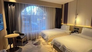 Ein Hotelzimmer mit zwei Betten, einem Schreibtisch, einem Stuhl und einem großen Fenster mit Vorhängen.