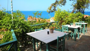 A terrace with tables and chairs, overlooking a coastal view. - Atlantis Rooms (Agios Konstantinos)