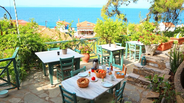 An outdoor patio with stone flooring, green furniture, and a table set for dining with a view of the sea. - Atlantis Rooms (Agios Konstantinos)
