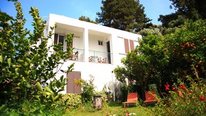 A white building with a balcony, surrounded by lush greenery and orange trees. - Atlantis Rooms (Agios Konstantinos)