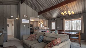 A cozy cabin interior with a large sofa, a dining table, and a kitchen area.
